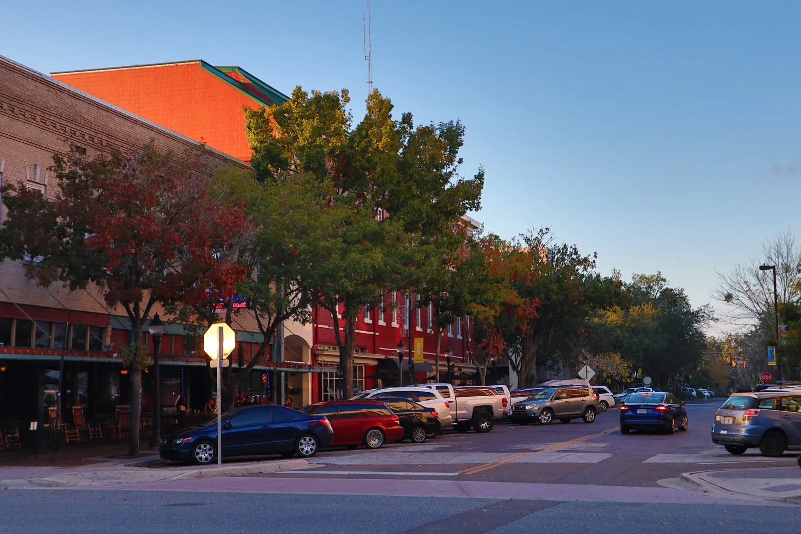 Restaurants and parked cars along a brick street in downtown Gainesville at dusk.