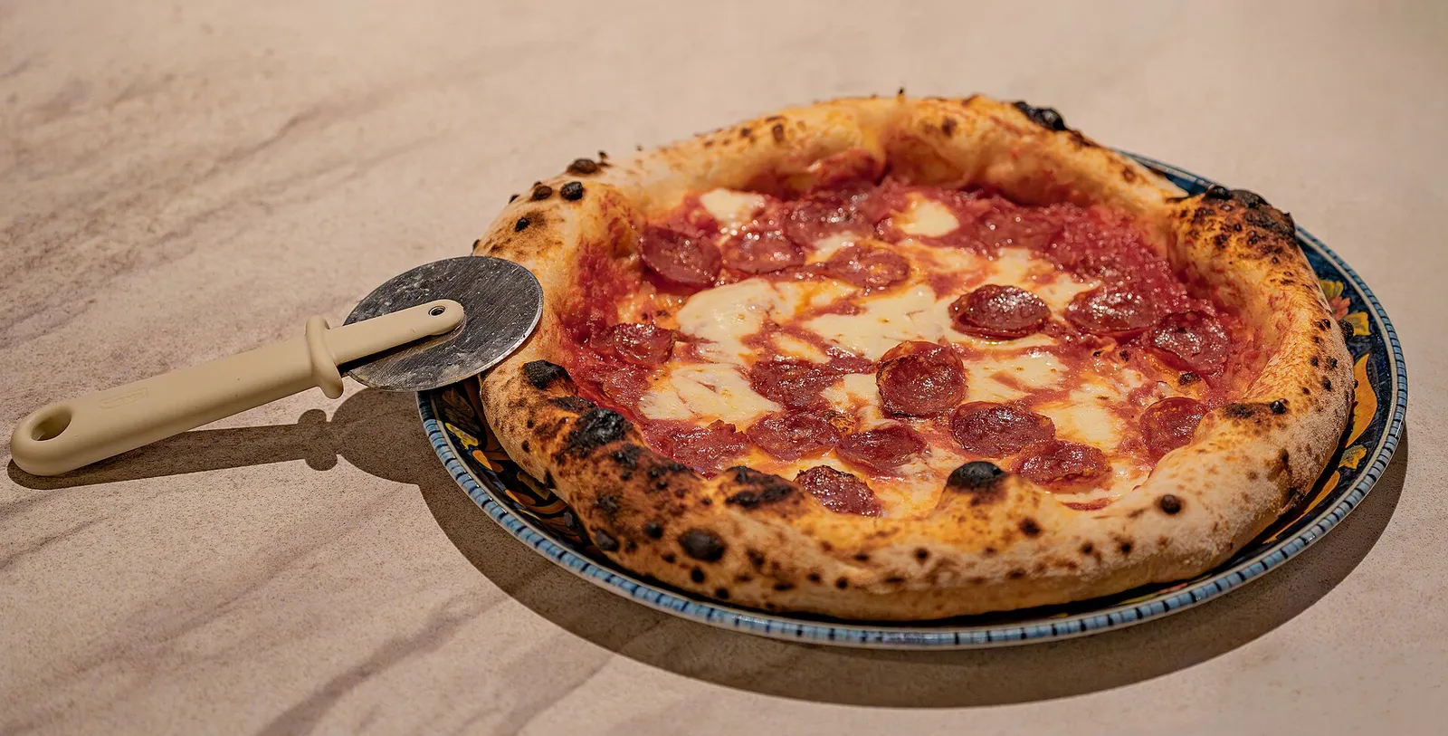 A wood-fired pepperoni pizza with a pizza cutter. The photo was not taken at a Gainesville restaurant.